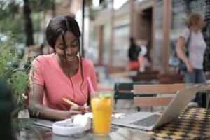 A young woman writing with headphones and music at a cafe